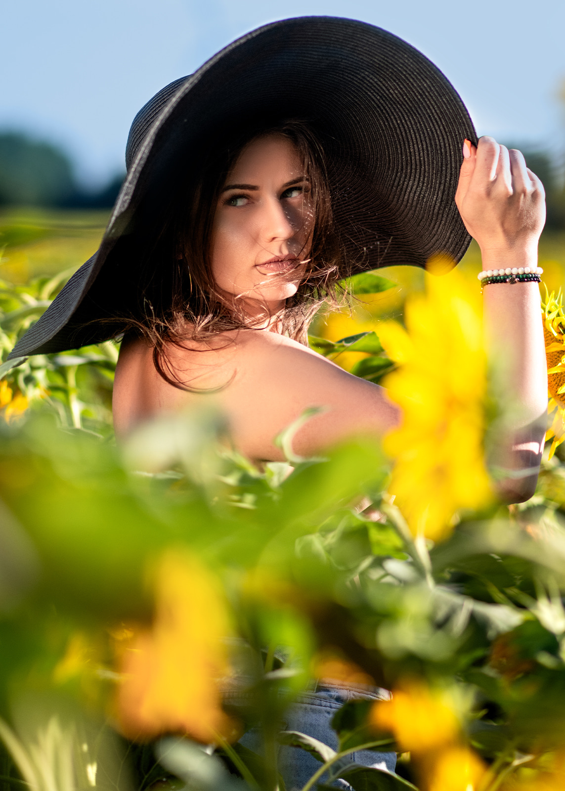 Woman wearing a large black hat among sunflowers in golden evening light.