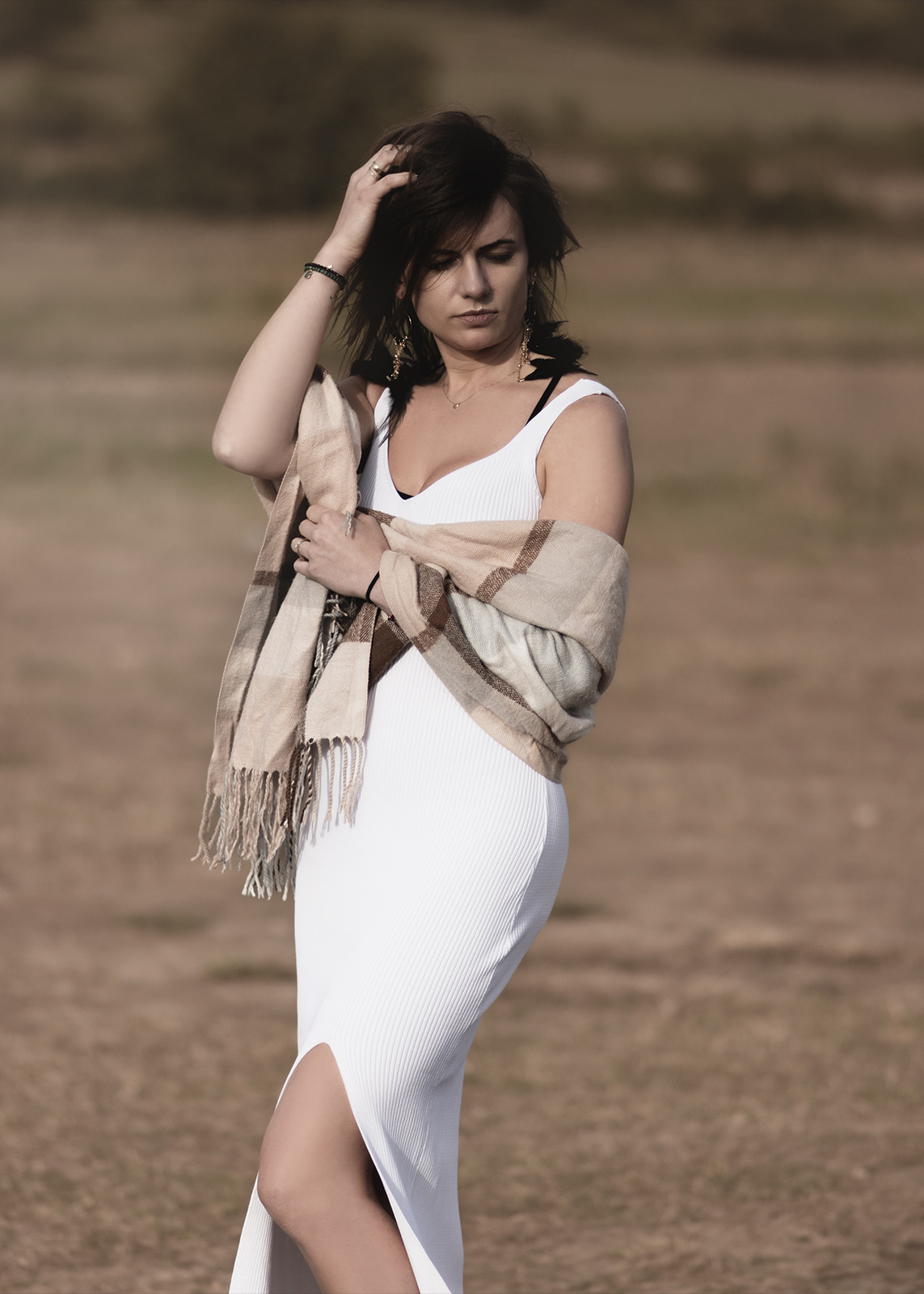 Brunette woman standing outdoors wrapped in a light shawl during golden hour.