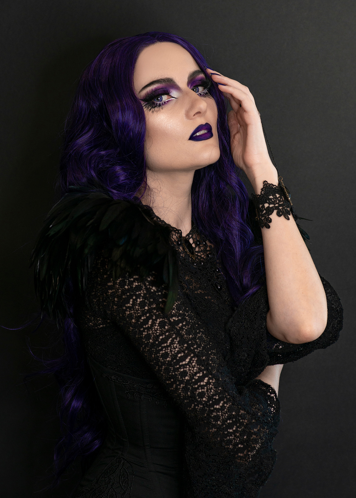 Woman with violet hair and dramatic makeup posing against a dark background.