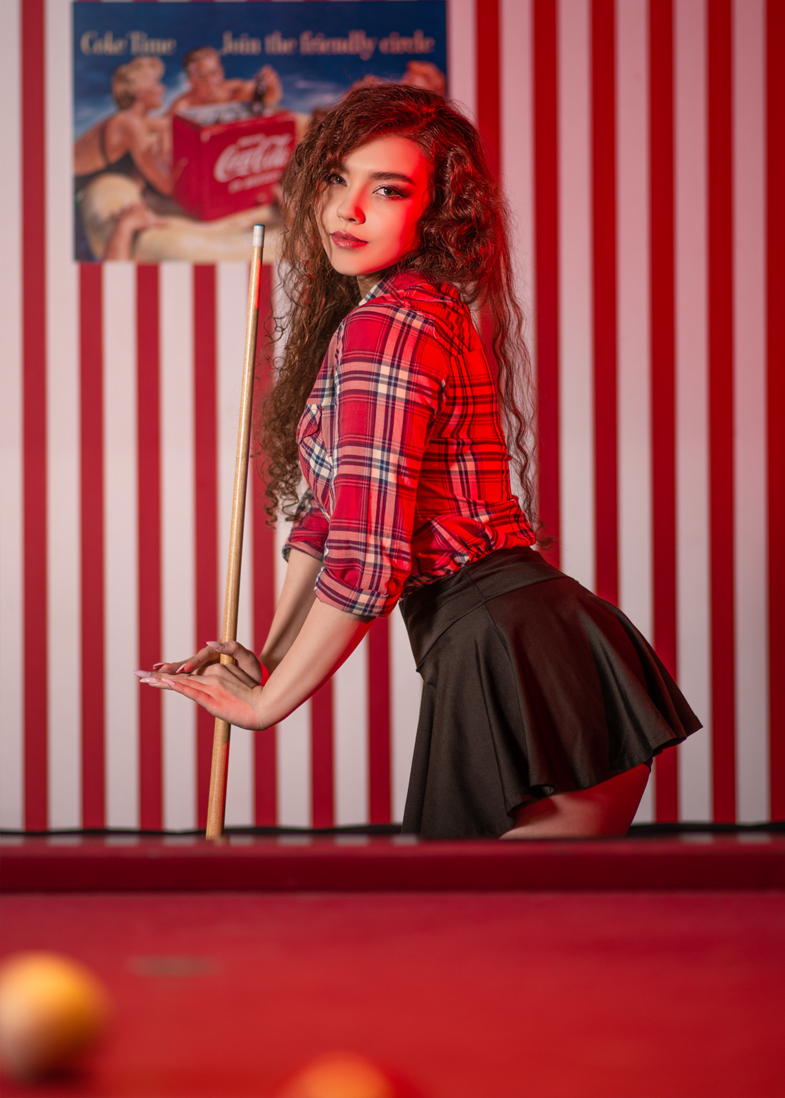 Curly-haired woman posing against a red and white striped wall.