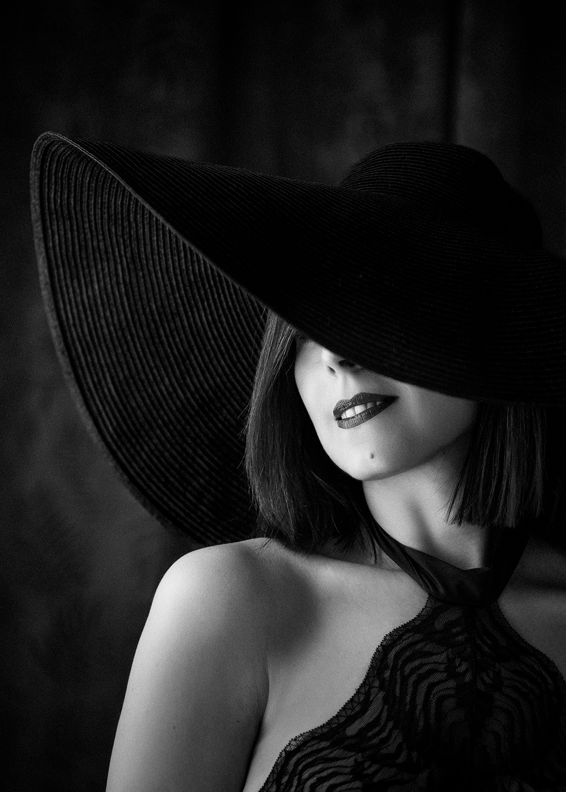 Black and white portrait of a woman wearing a large black hat covering part of her face.