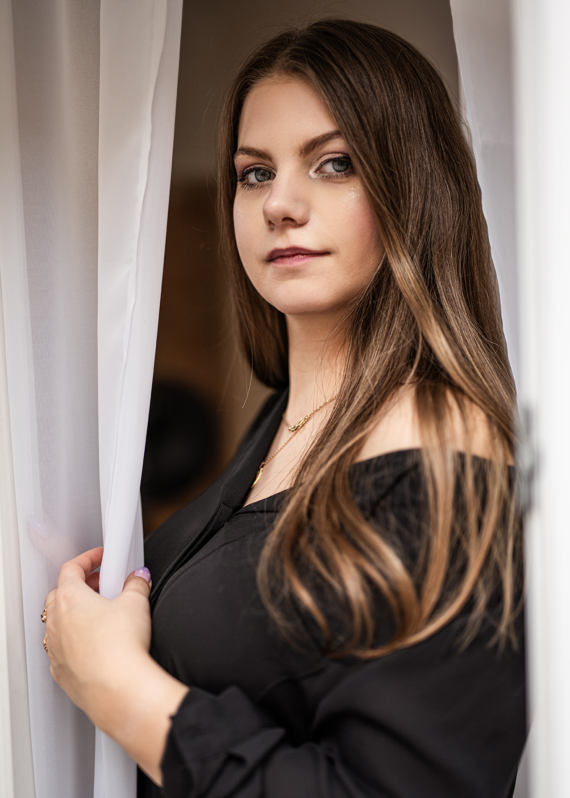 Portrait of a young brunette woman standing beside white curtains.