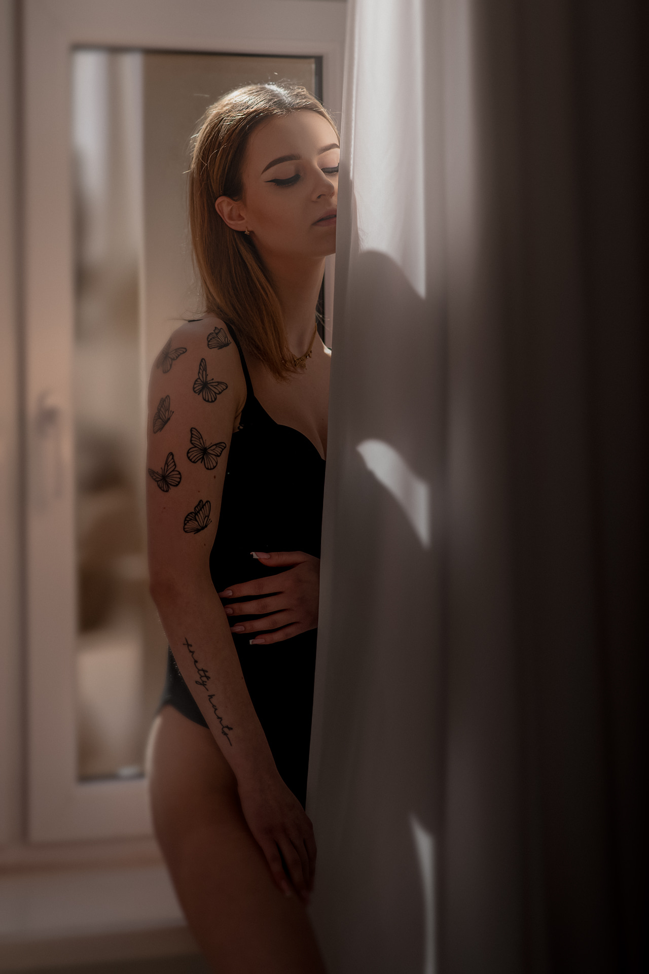 Woman standing beside a large window wearing elegant black lingerie.
