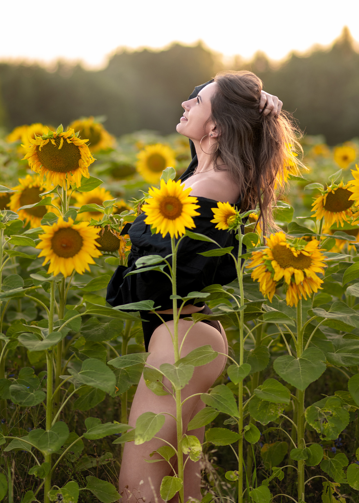 Woman standing among blooming sunflowers illuminated by warm golden sunset light.