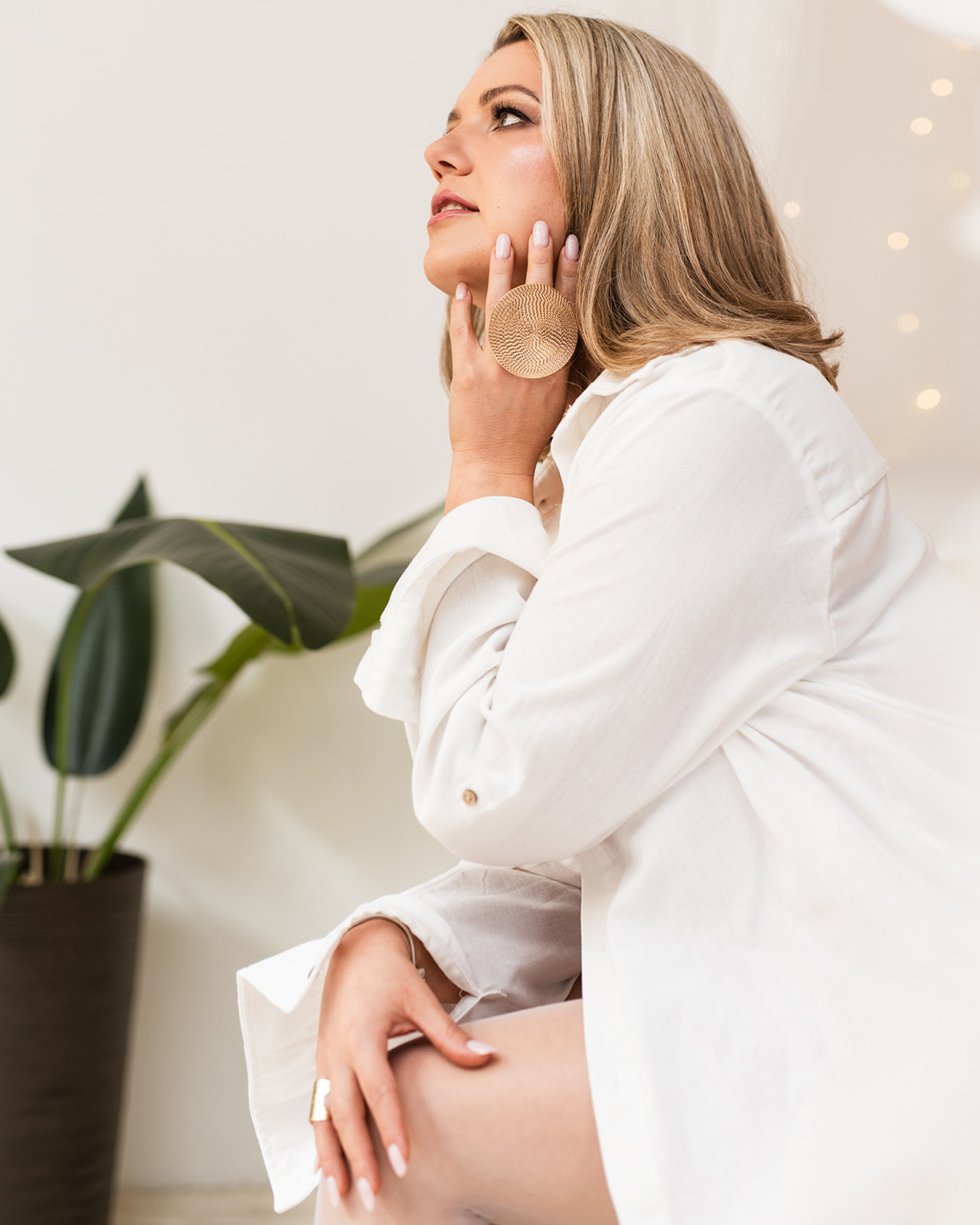 Blonde woman wearing a white blouse looking upward in warm natural light.