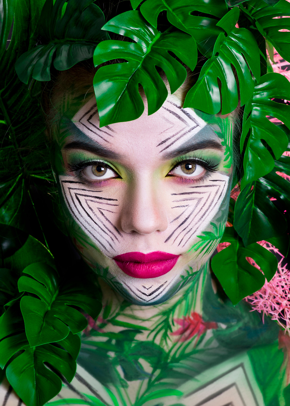 Woman with green artistic makeup surrounded by tropical leaves.