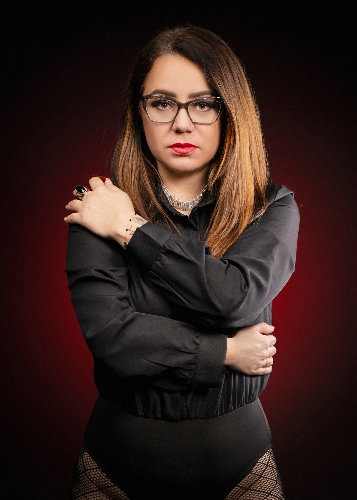 Woman wearing glasses and a black blouse photographed against a dark background with subtle red light.