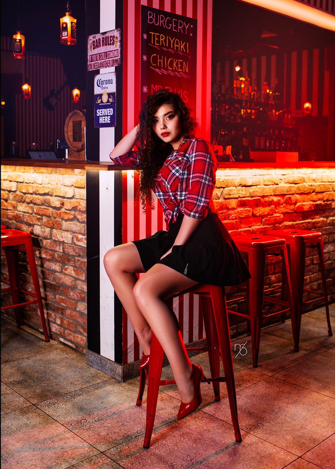 Woman sitting in a restaurant illuminated by warm red and orange neon lights.