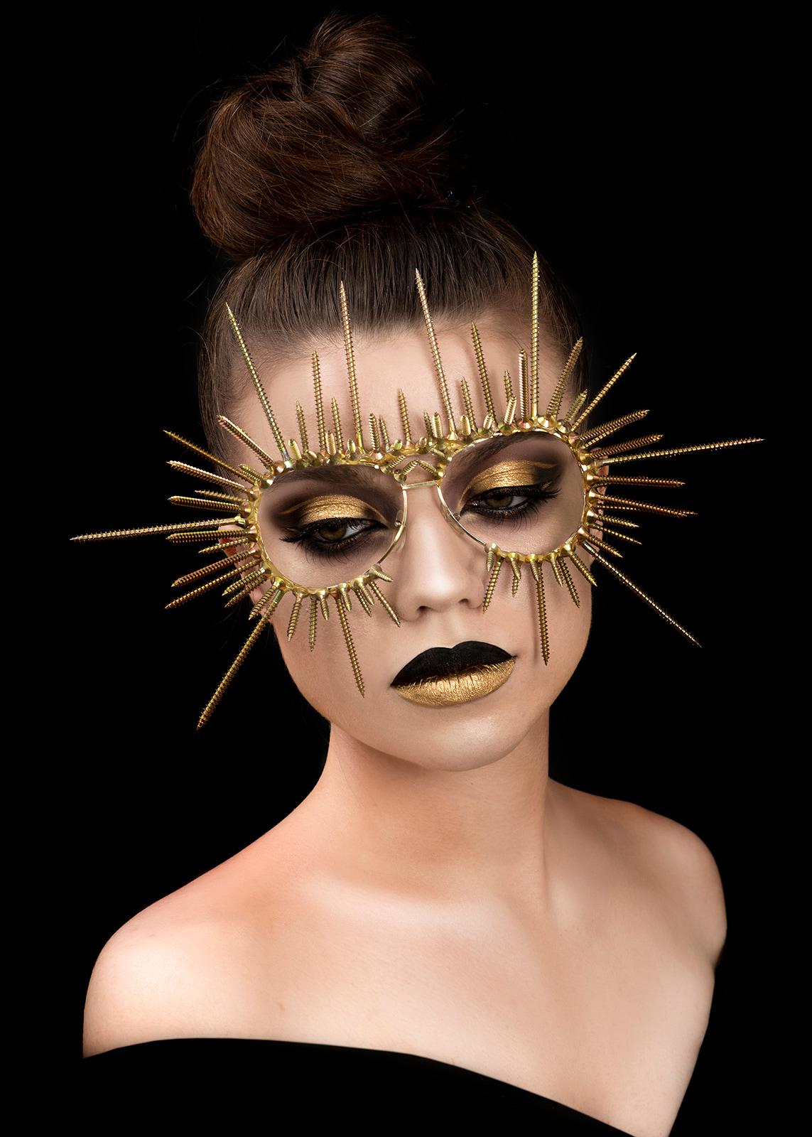 Woman wearing a gold sun-shaped mask with dramatic black and gold makeup.