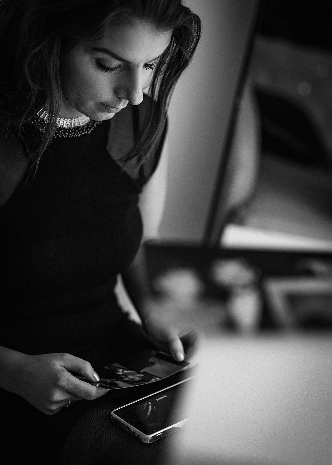 Black and white portrait of a woman illuminated by soft directional light, looking downward in a contemplative pose.