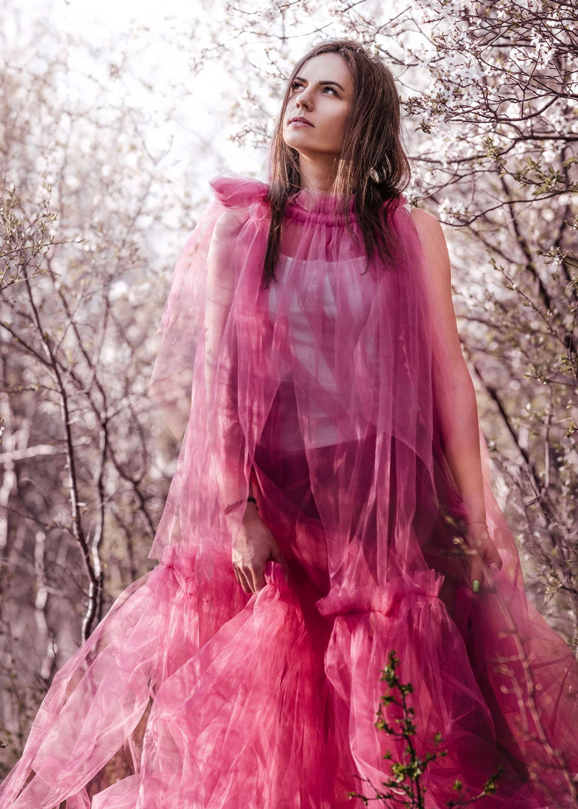 Woman wearing a flowing pink dress standing among blossoming trees.