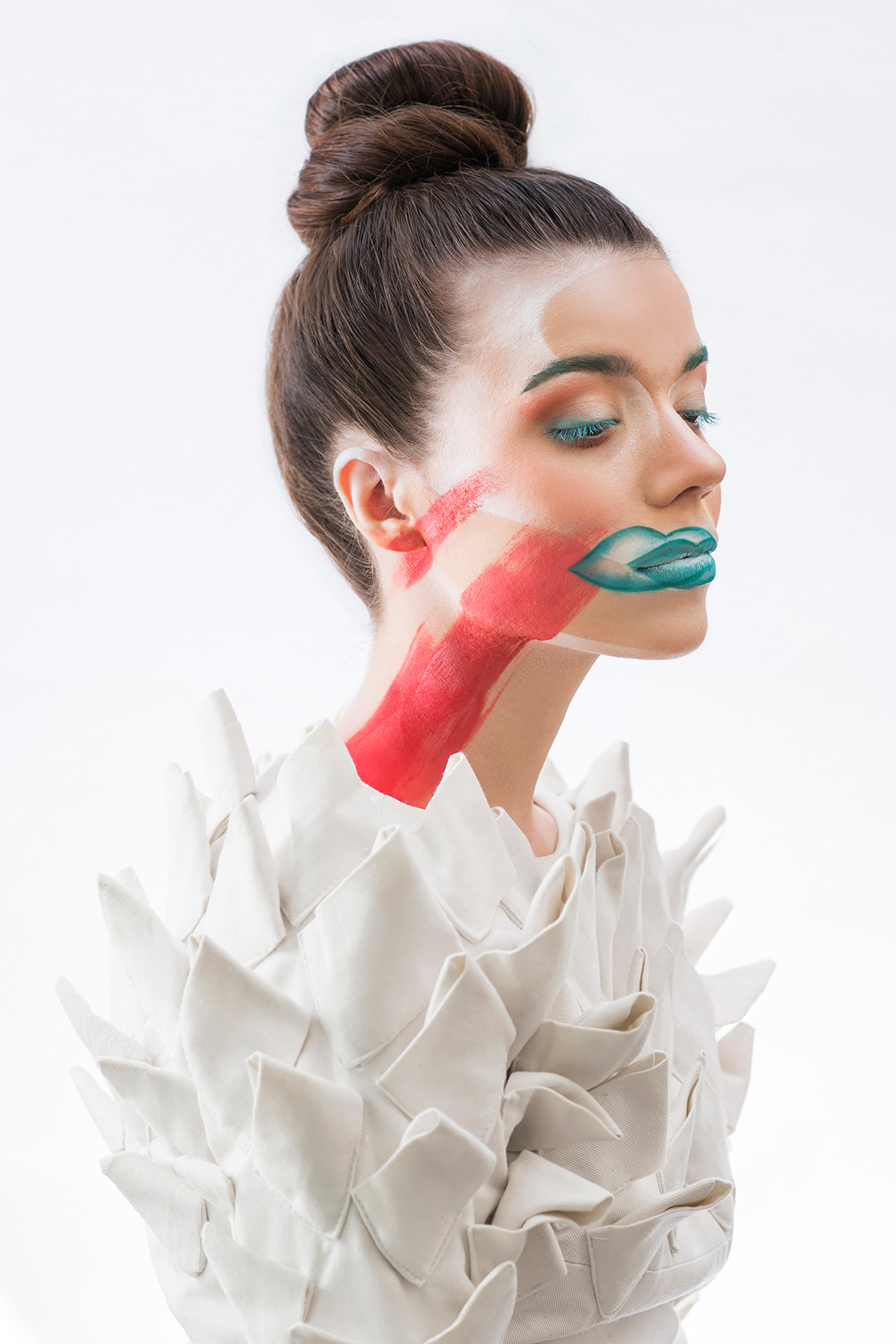 Beauty portrait of a woman with artistic red and turquoise face paint against a white background.