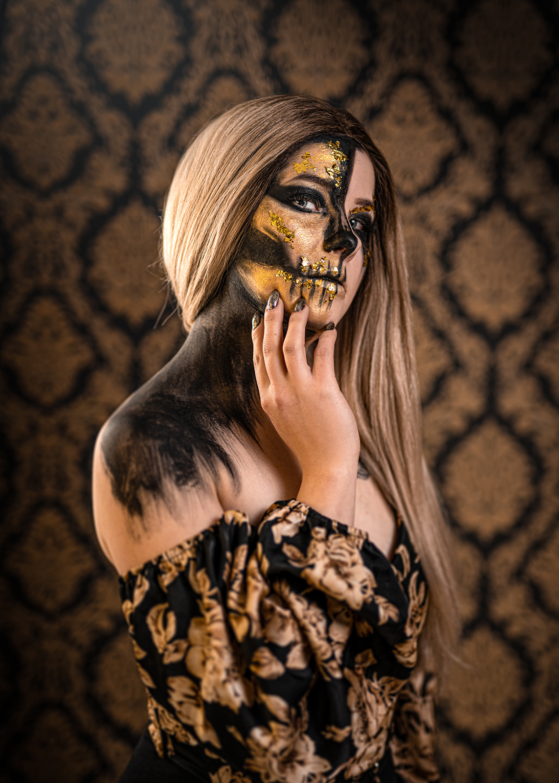 Woman with black and gold artistic body paint posing against an ornamental background.