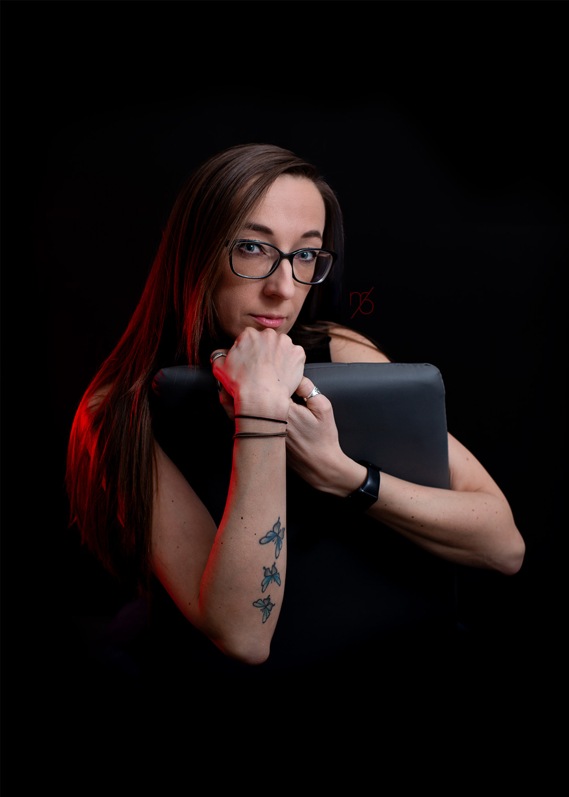 Portrait of a woman wearing glasses against a dark background with red accent lighting.