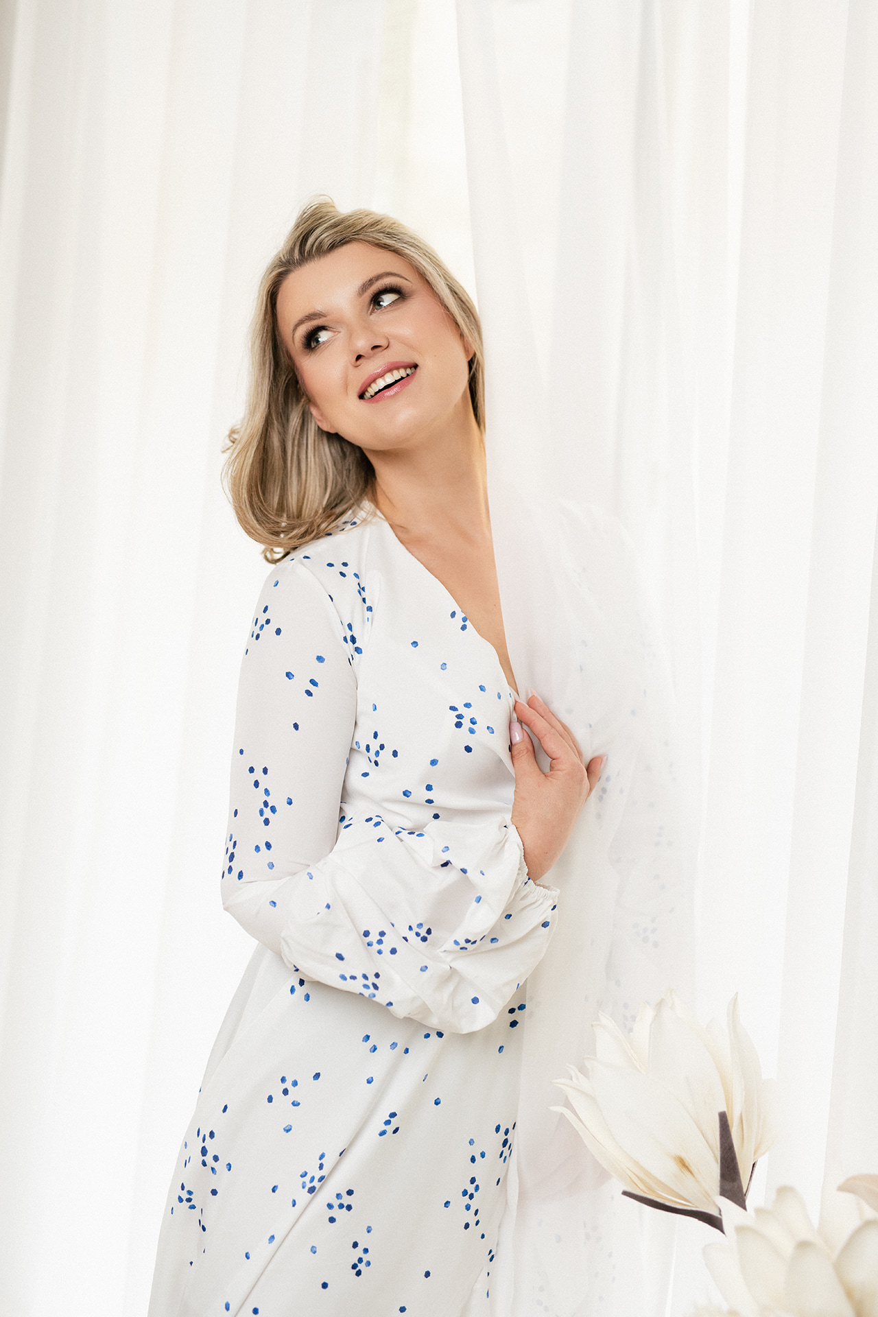 Blonde woman in a white floral dress smiling while looking upward.