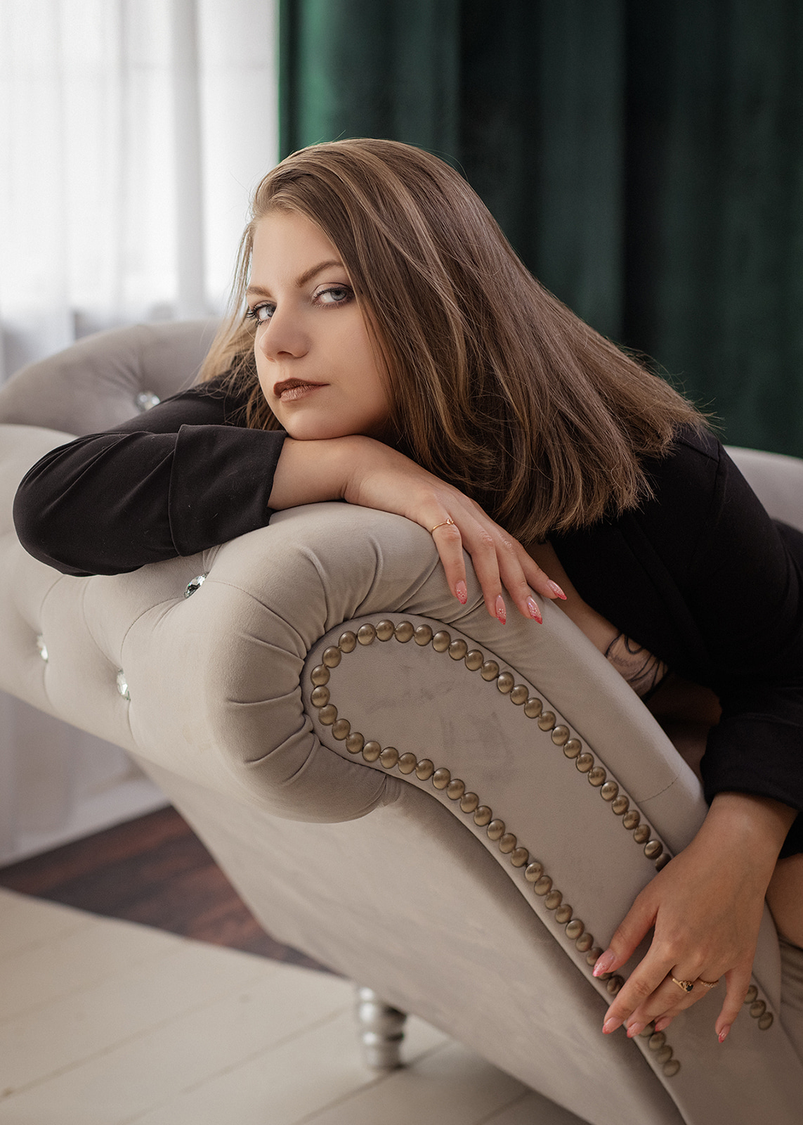 Young brunette woman resting her head on a sofa in soft window light.